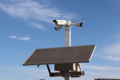 Câmera de vigilância instalada em poste com painel solar, contra o céu azul.